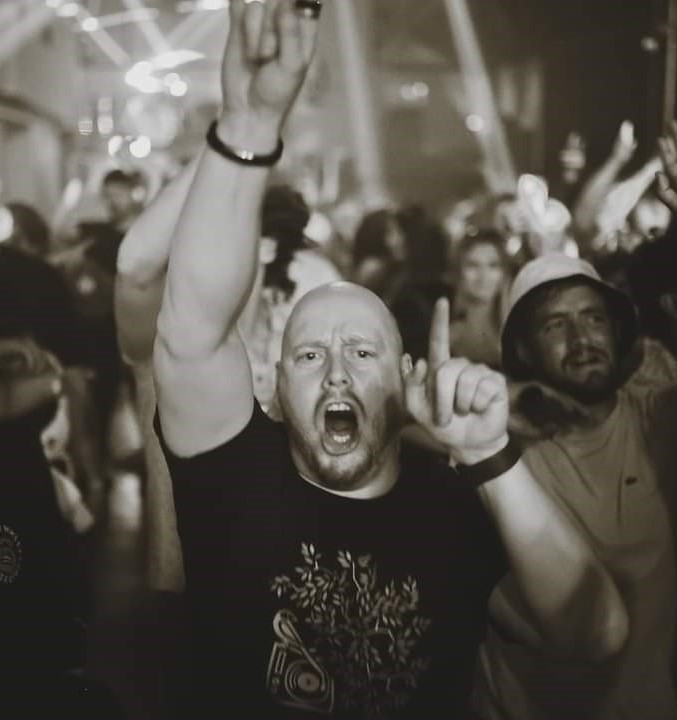 people in a crowd, one man in front looking at the camera shouting and holding his pointer finger up