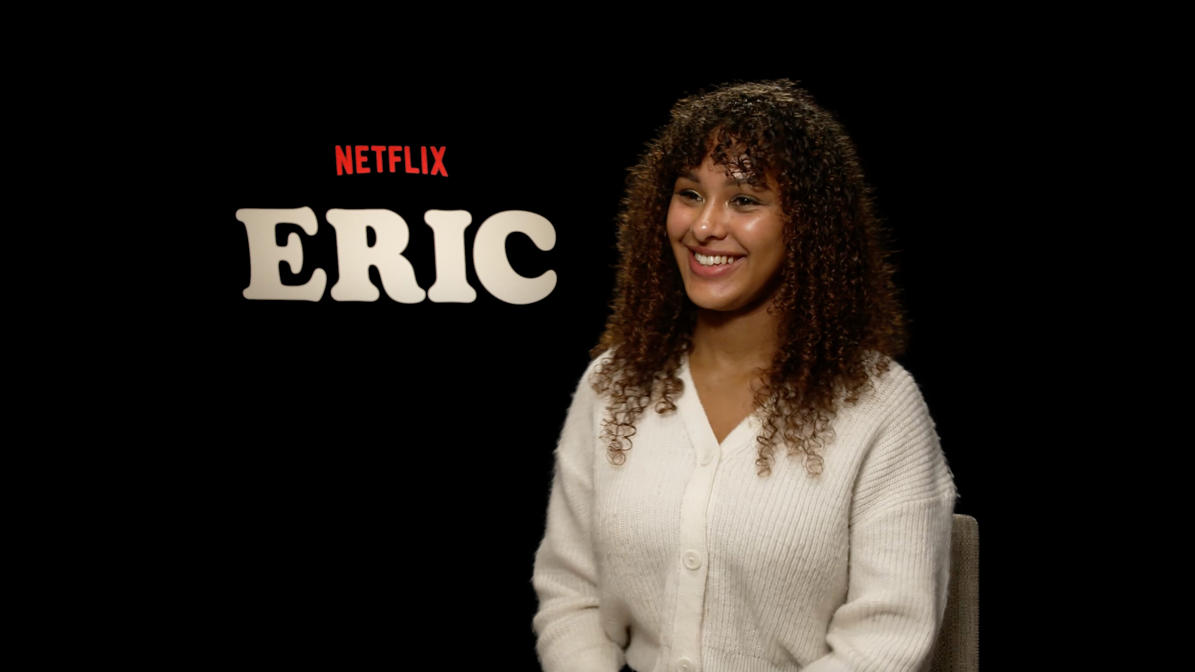 Alleyah sitting in front of a black background with the word "Eric" behind her