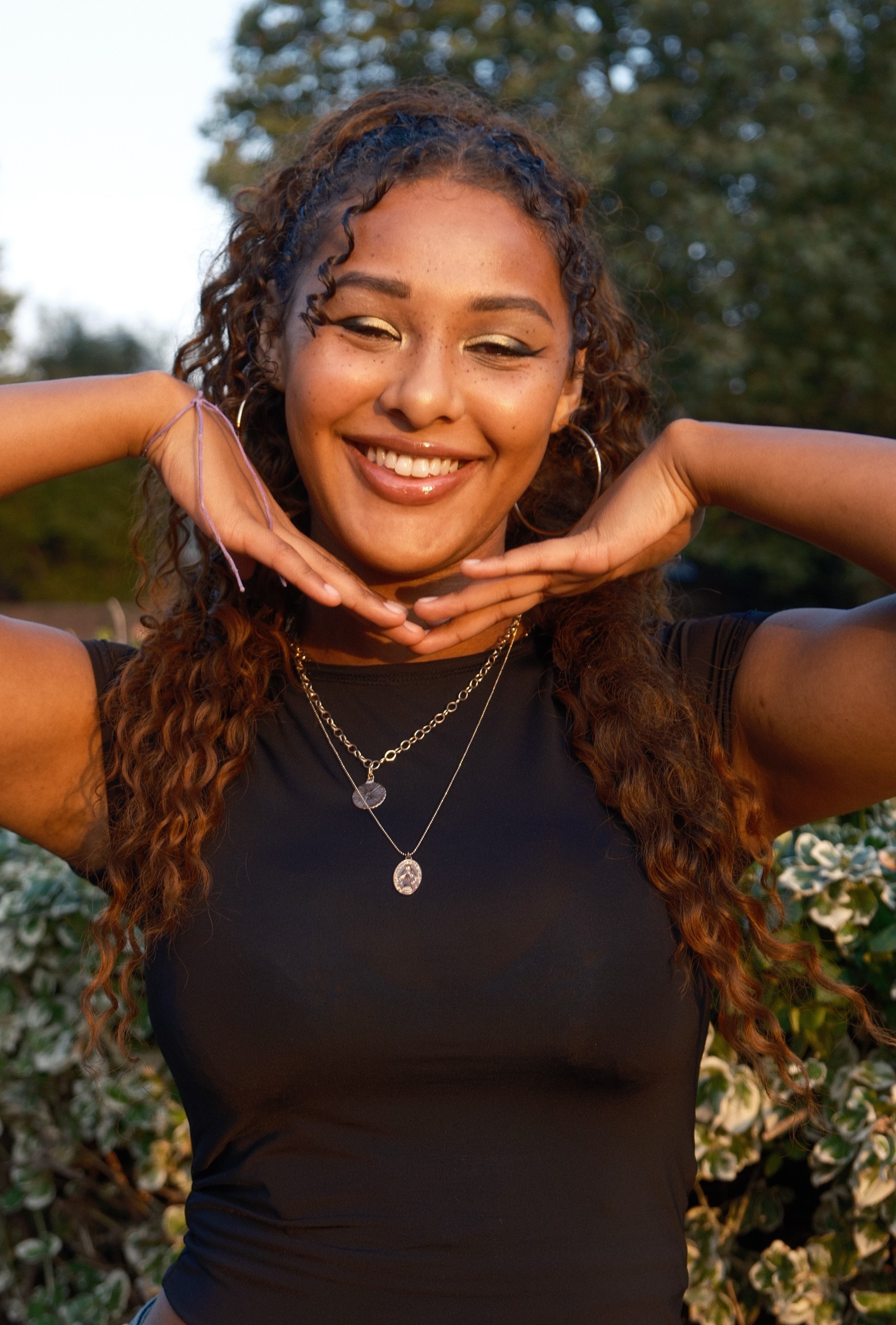 Alleyah smiling at the camera while holding her hands up to her face, wearing a black shirt