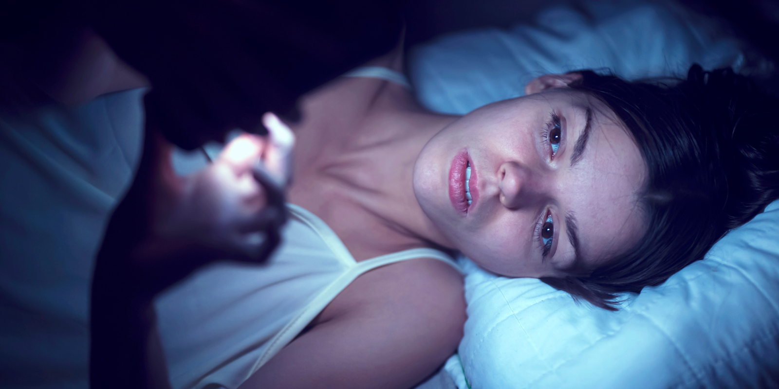 woman lying in bed looking at her phone