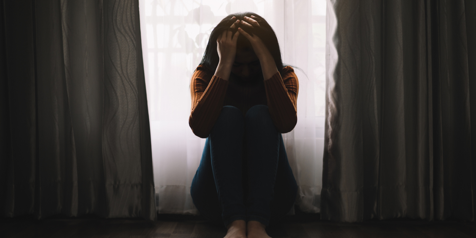 young woman sitting on the floor with her face in her hands