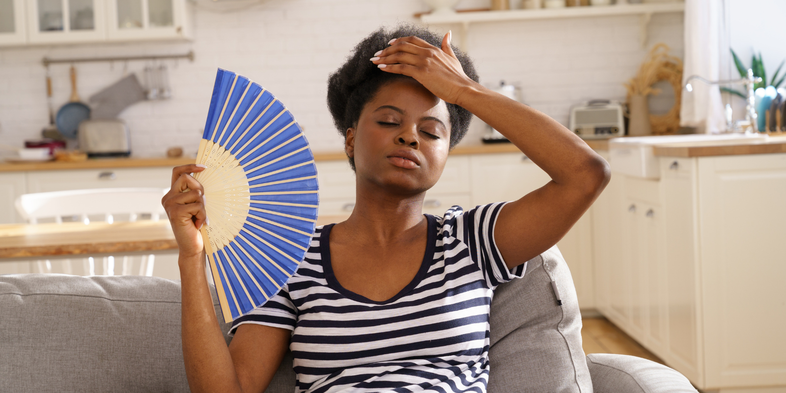 woman sitting on a couch using a paper fan to cool herself off 