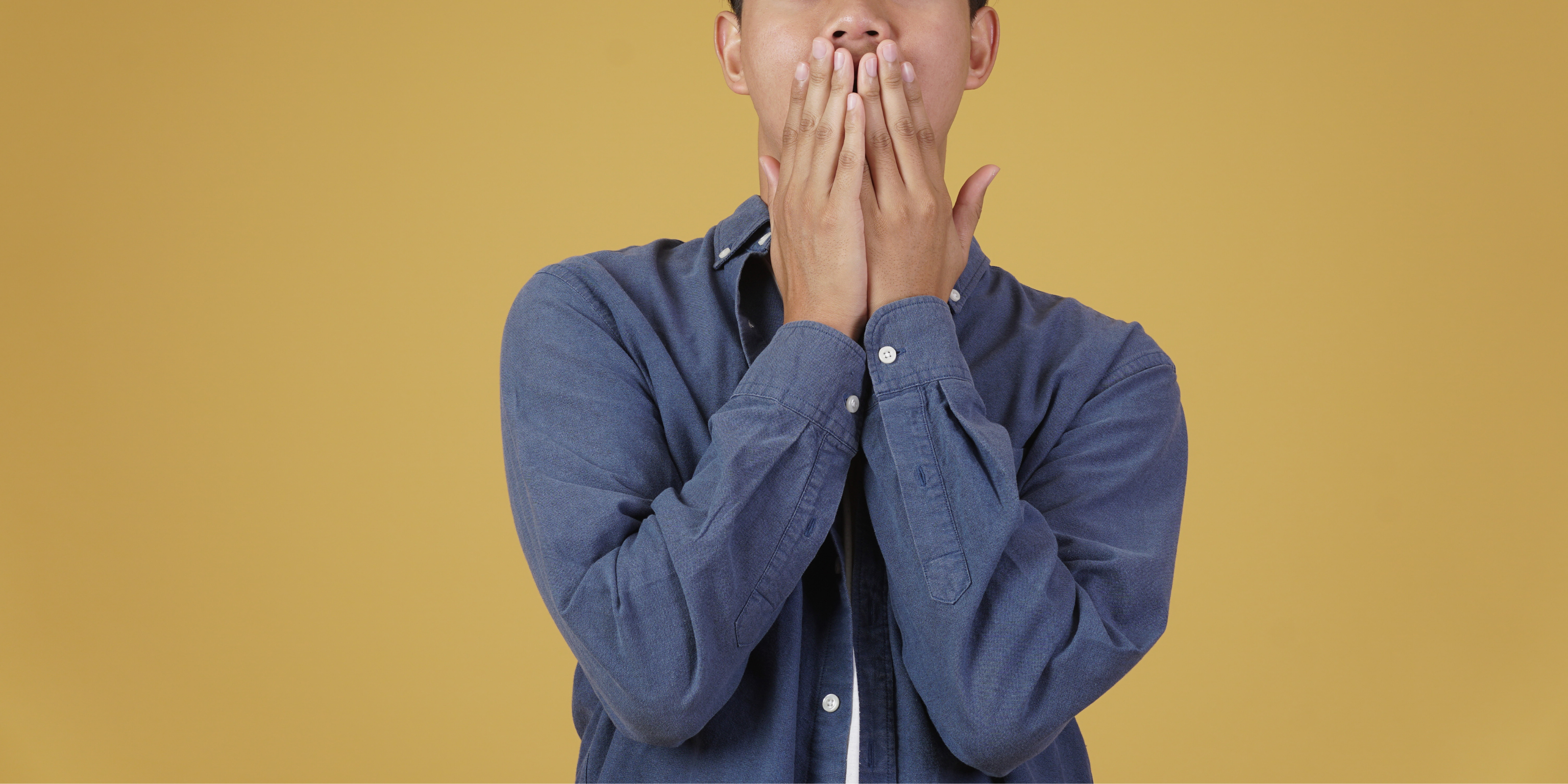 a boy covering his mouth with both hands on a yellow background