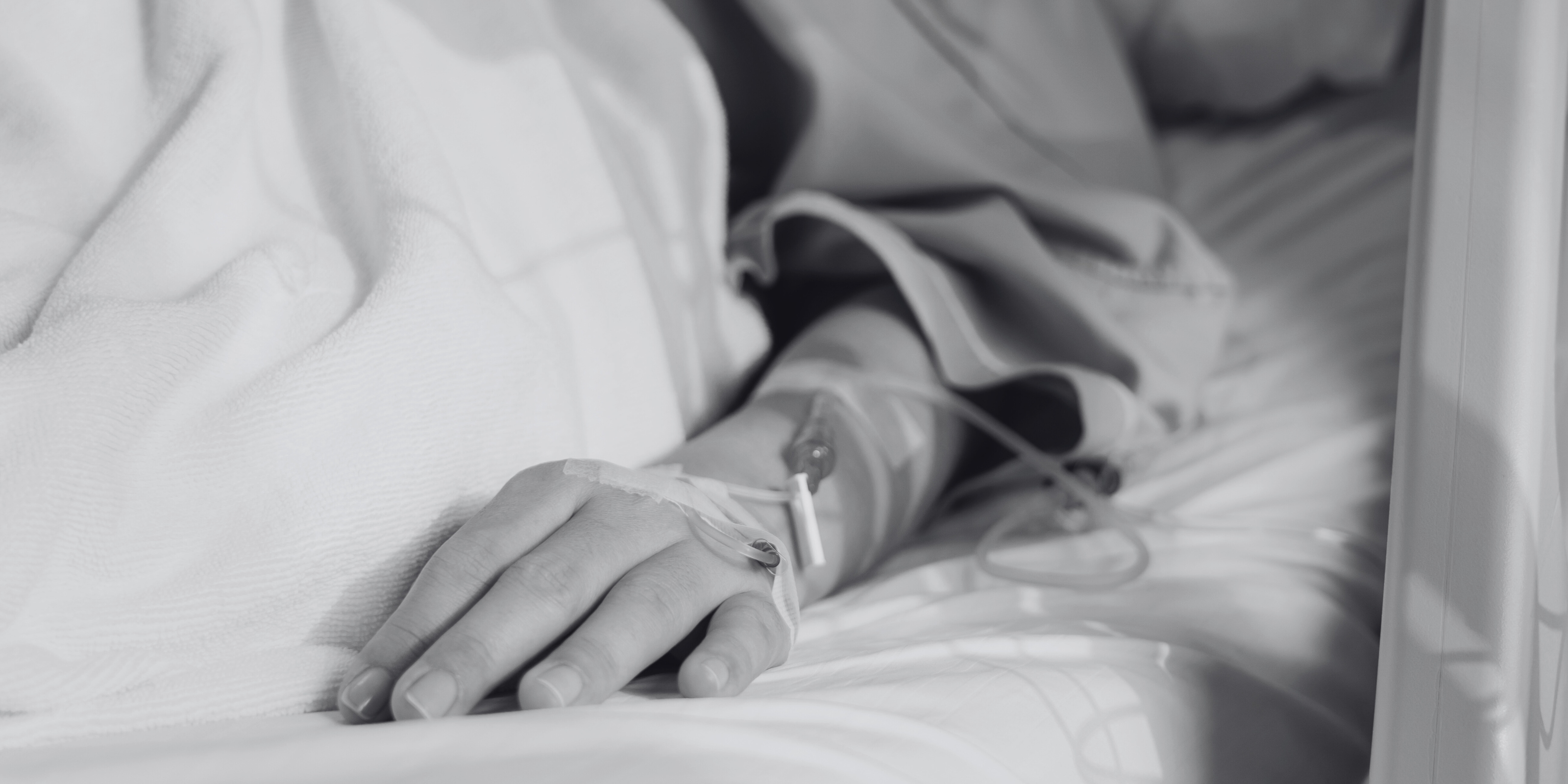 a black and white image of a persons arm hooked up to IVs who is lying in a hospital bed