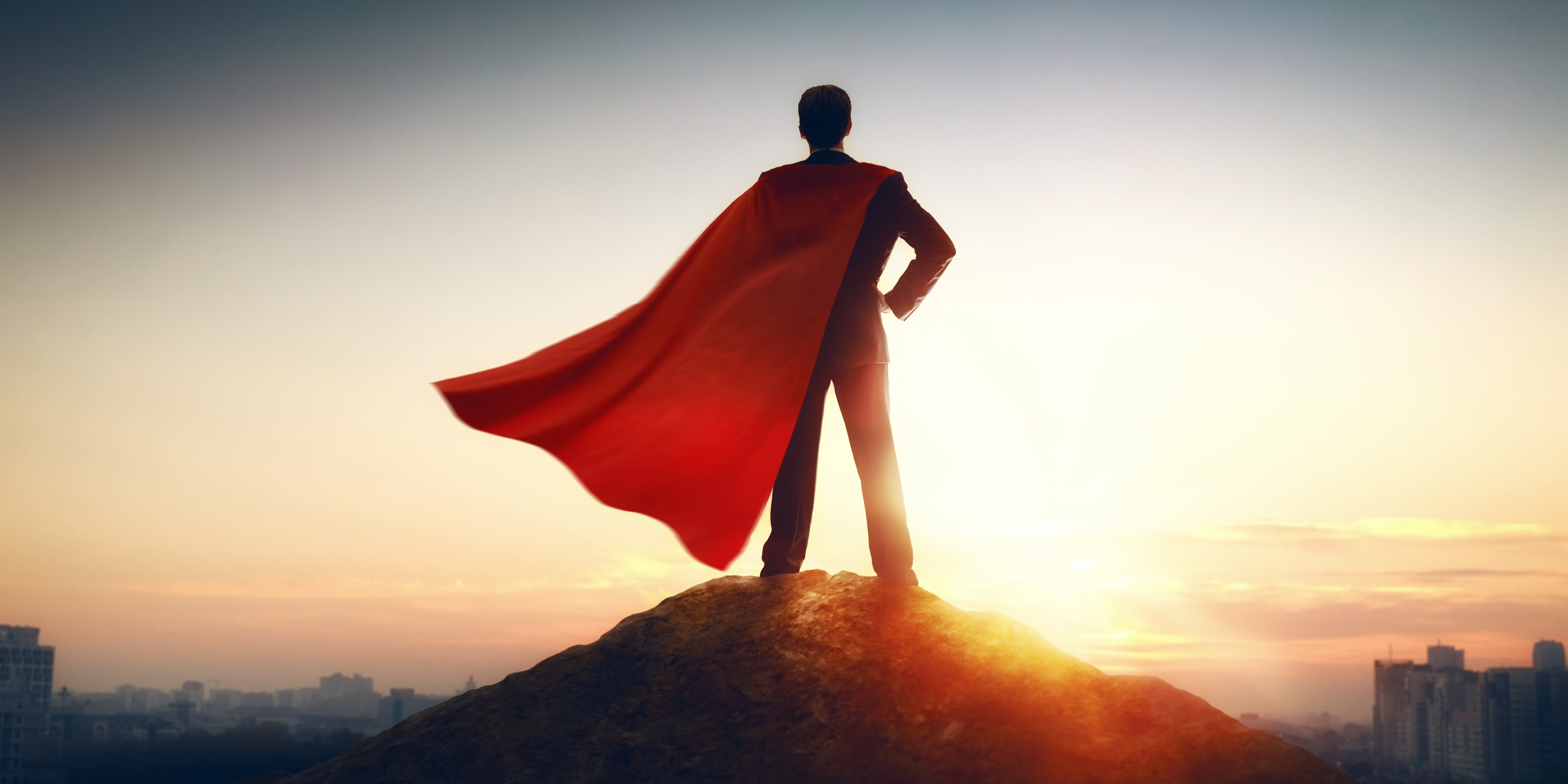 a man in a suit and a red cape standing on a hill looking out over a city