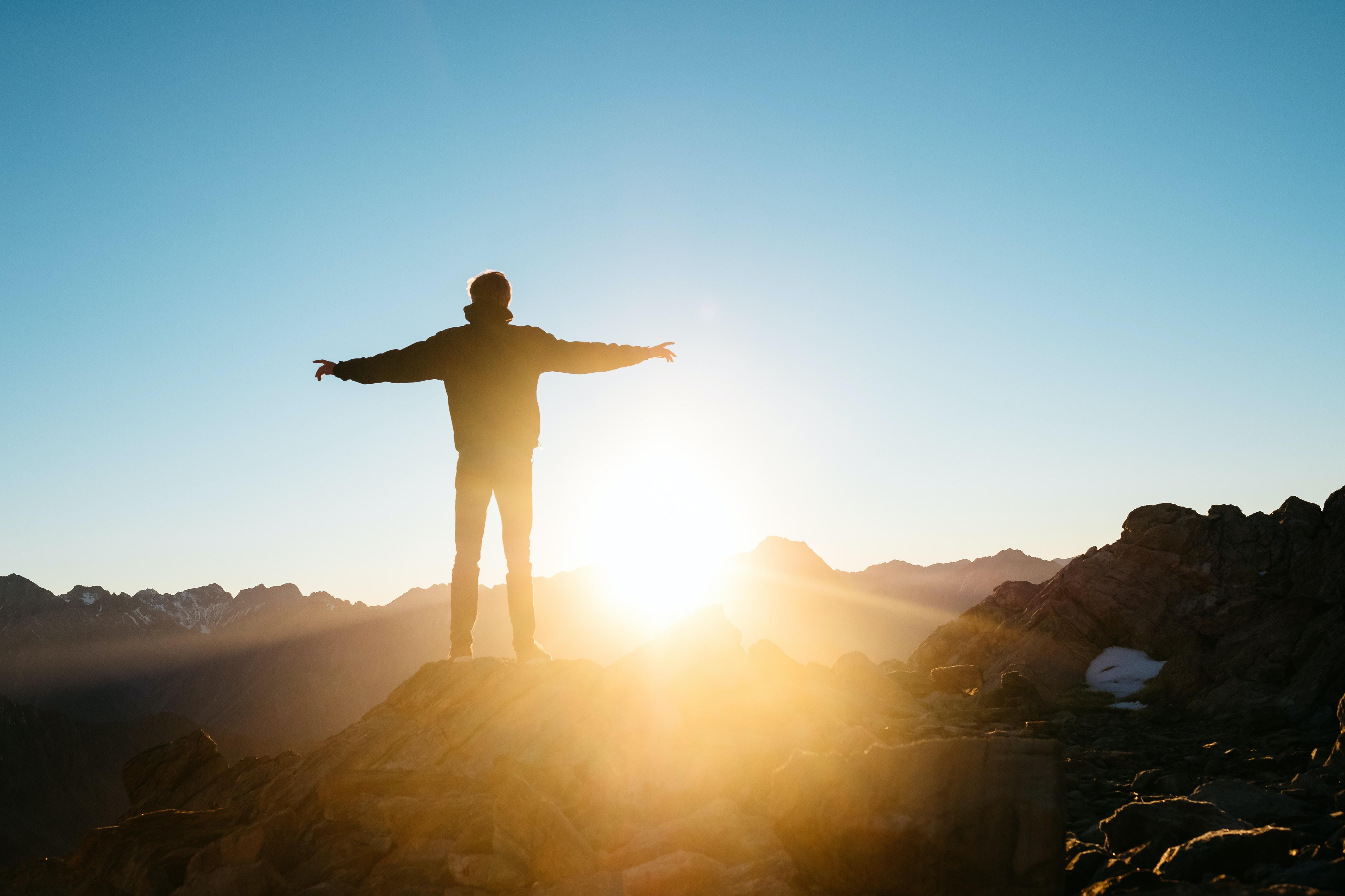 person standing on a hill with their arms stretched out in front of a sunrise
