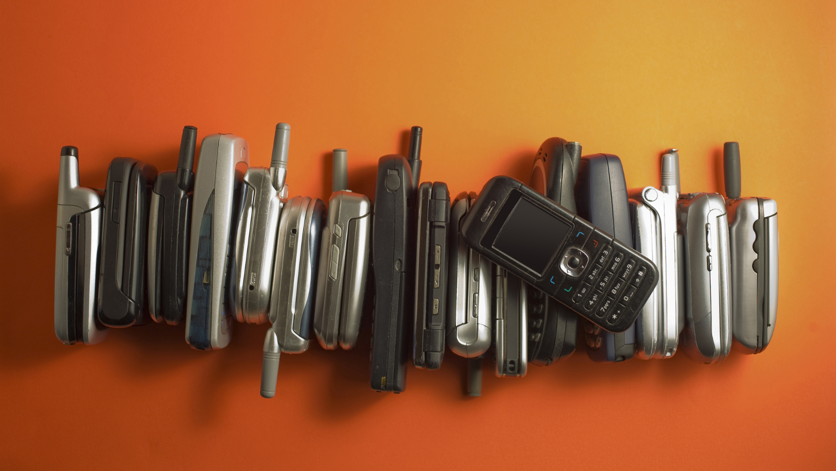 a pile of flip phones on an orange background