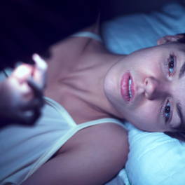 woman lying in bed looking at her phone