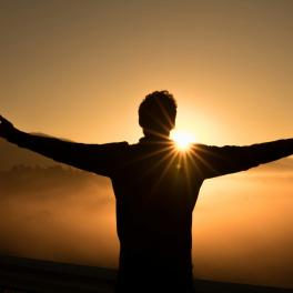 man standing with his arms stretched out at sunset
