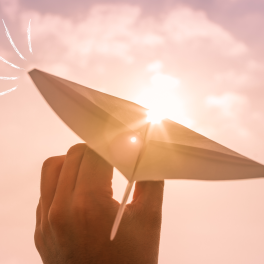 paper airplane being held against a pink sky