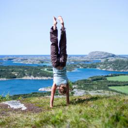 person doing a handstand on a hill overlooking water