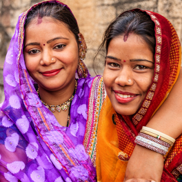Three young women in colorful garb standing together smiling at the camera