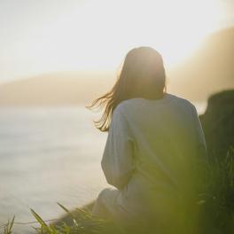 woman sitting on a cliff overlooking the water