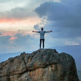 man standing with his harms stretched out on a cliff 