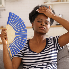 woman sitting on a couch using a paper fan to cool herself off 
