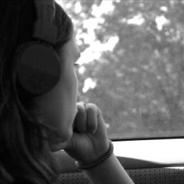 young person looking out the window of a car with headphones on, grayscale