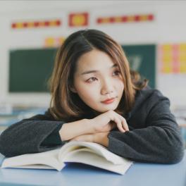 young woman resting her head on a book in a classroom
