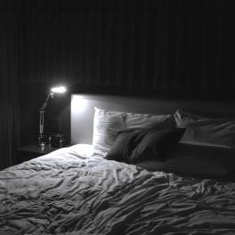 a black and white image of a dark bedroom with a lap shining on the beside table