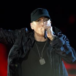 Eminem performing while wearing a black shirt, jacket and hat