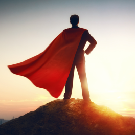 a man in a suit and a red cape standing on a hill looking out over a city