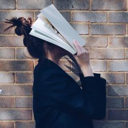 a woman wearing a bun and covering her face with a book 