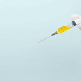 an image of a hand holding a syringe filled with a yellow liquid