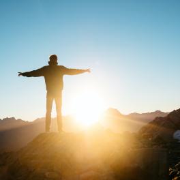 person standing on a hill with their arms stretched out in front of a sunrise