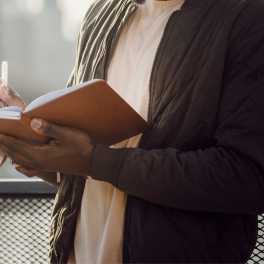 man standing on a bridge writing in a notebook
