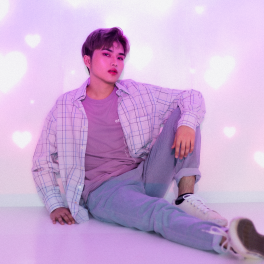 A photo of a k-pop inspired man sitting up against a wall