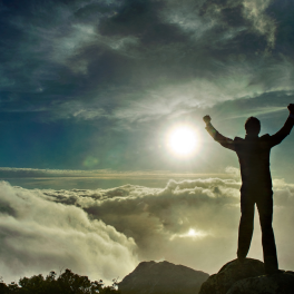 A man standing on top of a cliff with his arms raised in triumph