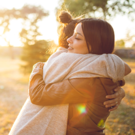 two females hugging in a grassy area
