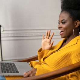 black woman on a video call waving at a laptop