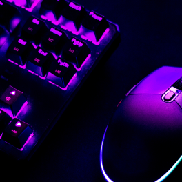 A keyboard and mouse in a dark room lit up with purple backlights
