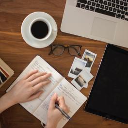 an overview photo of a person writing in a journal on a desk