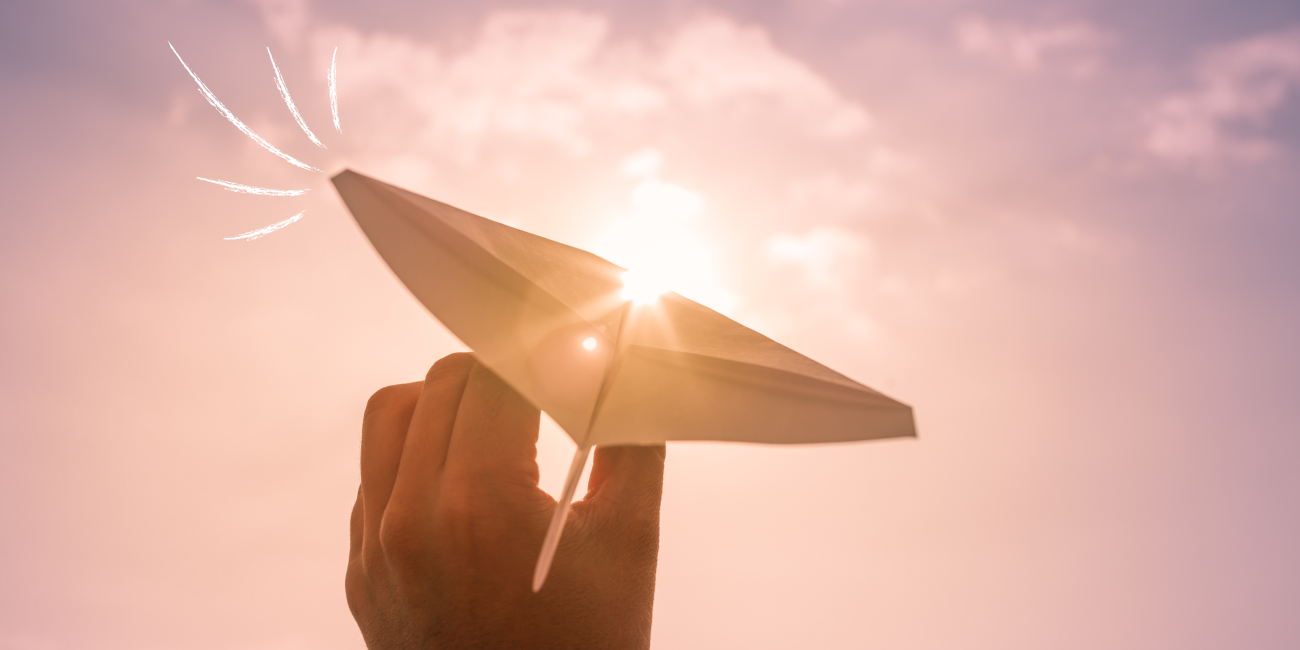 paper airplane being held against a pink sky
