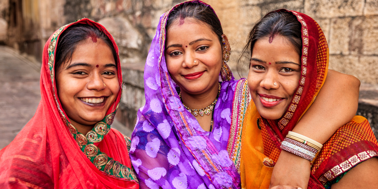 Three young women in colorful garb standing together smiling at the camera