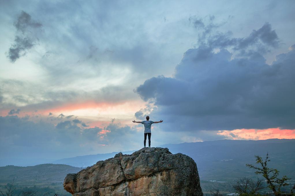 man standing with his harms stretched out on a cliff 