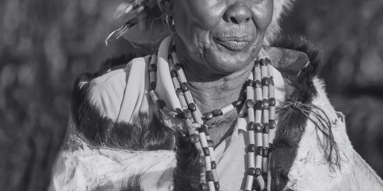 a black and white image of an elderly African woman wearing furs and necklaces