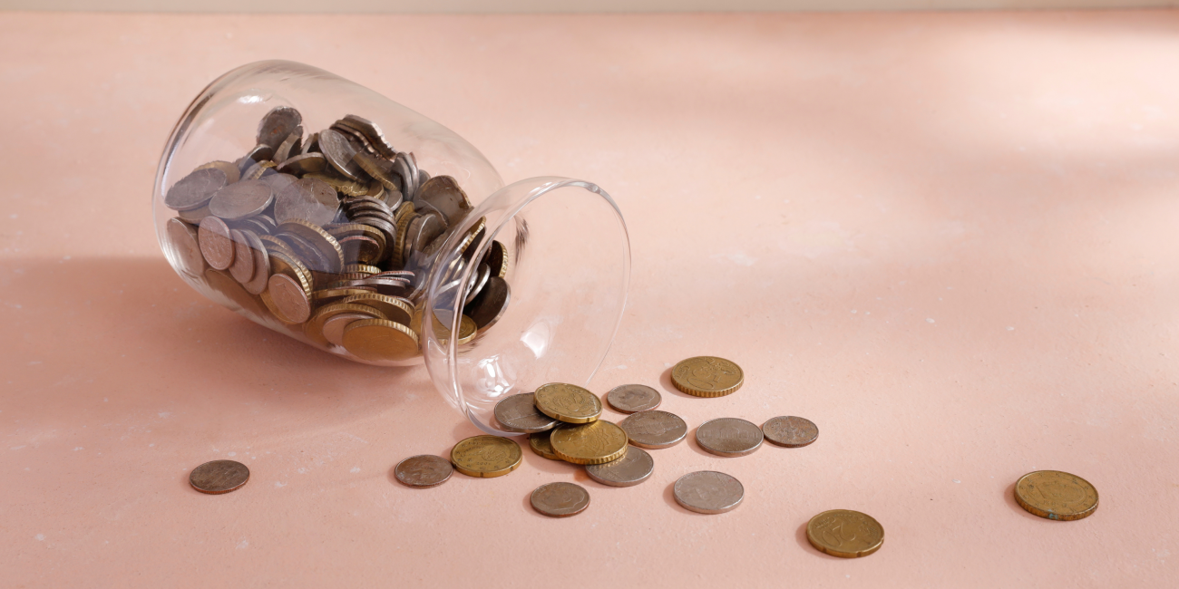 a jar of coins being spilled out on a pink surface