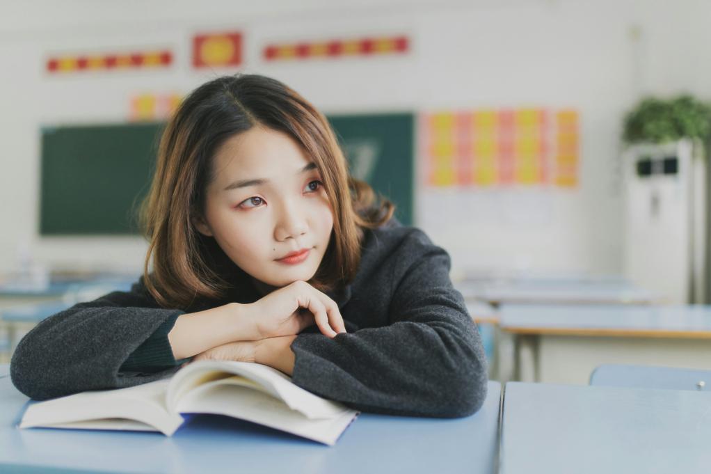 young woman resting her head on a book in a classroom