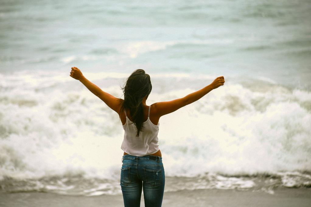 woman facing the ocean with her arms stretched out for the sky