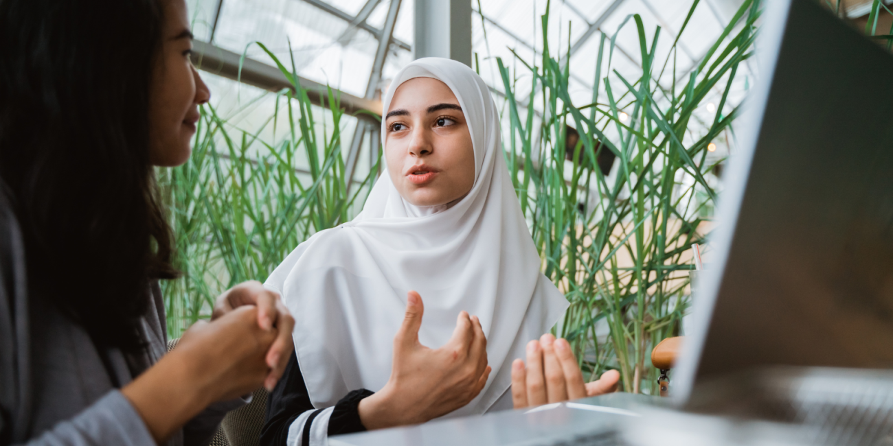 two young women having a conversation in front of a laptop