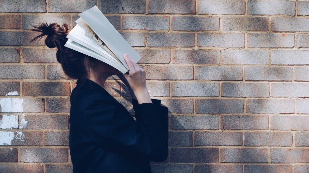 a woman wearing a bun and covering her face with a book 