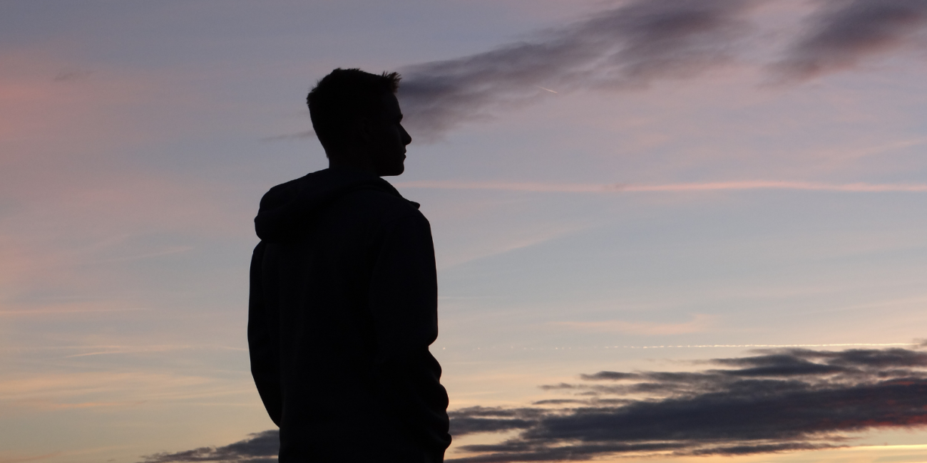 silhouette of young man staring out into sunset 