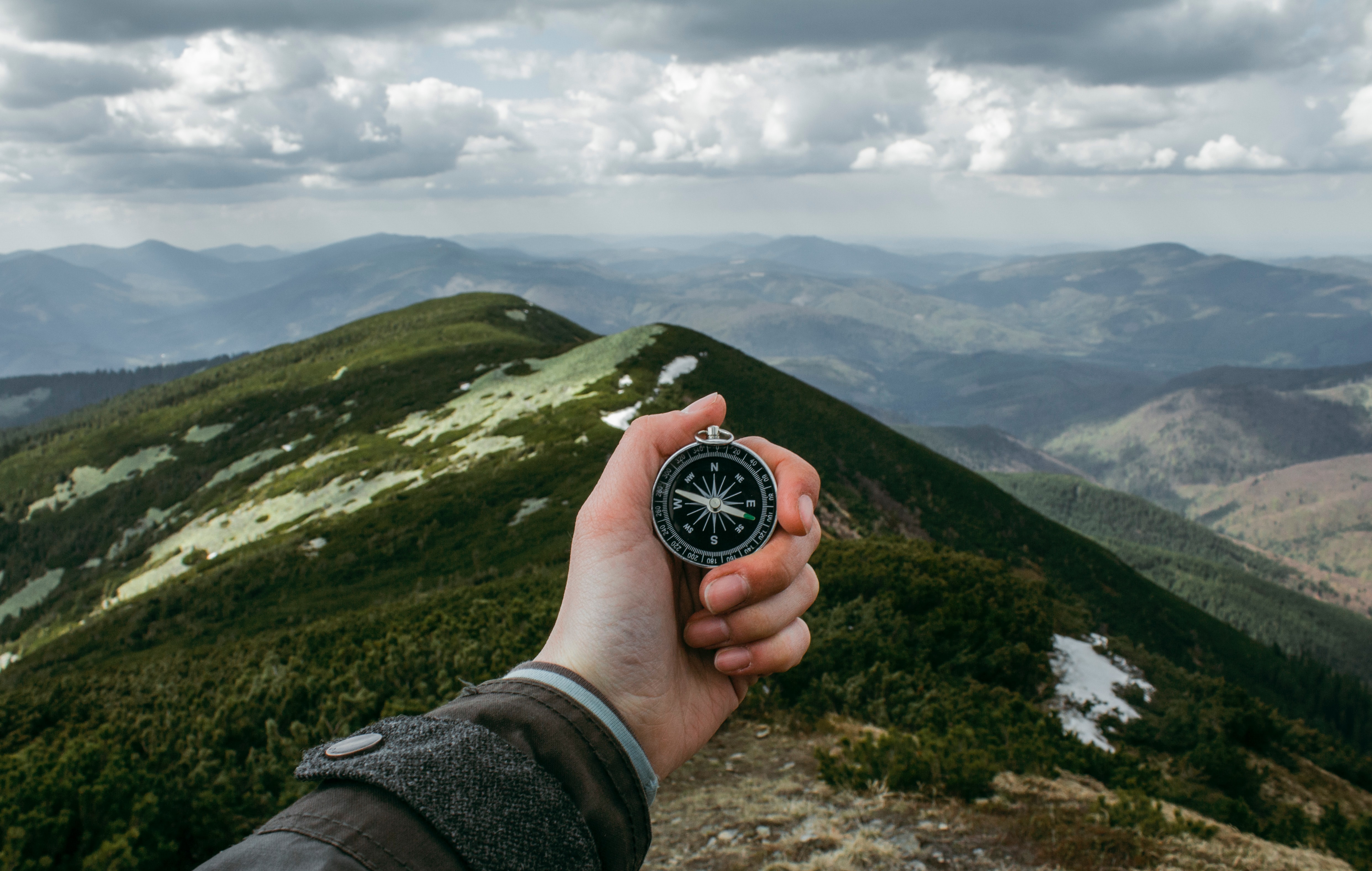 a hand holding out a compass over a mountain range