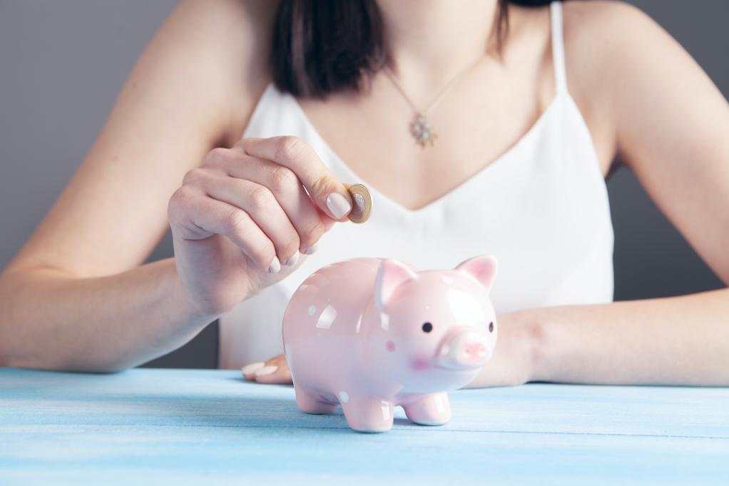 woman in a white tank top putting a coin into a piggy bank