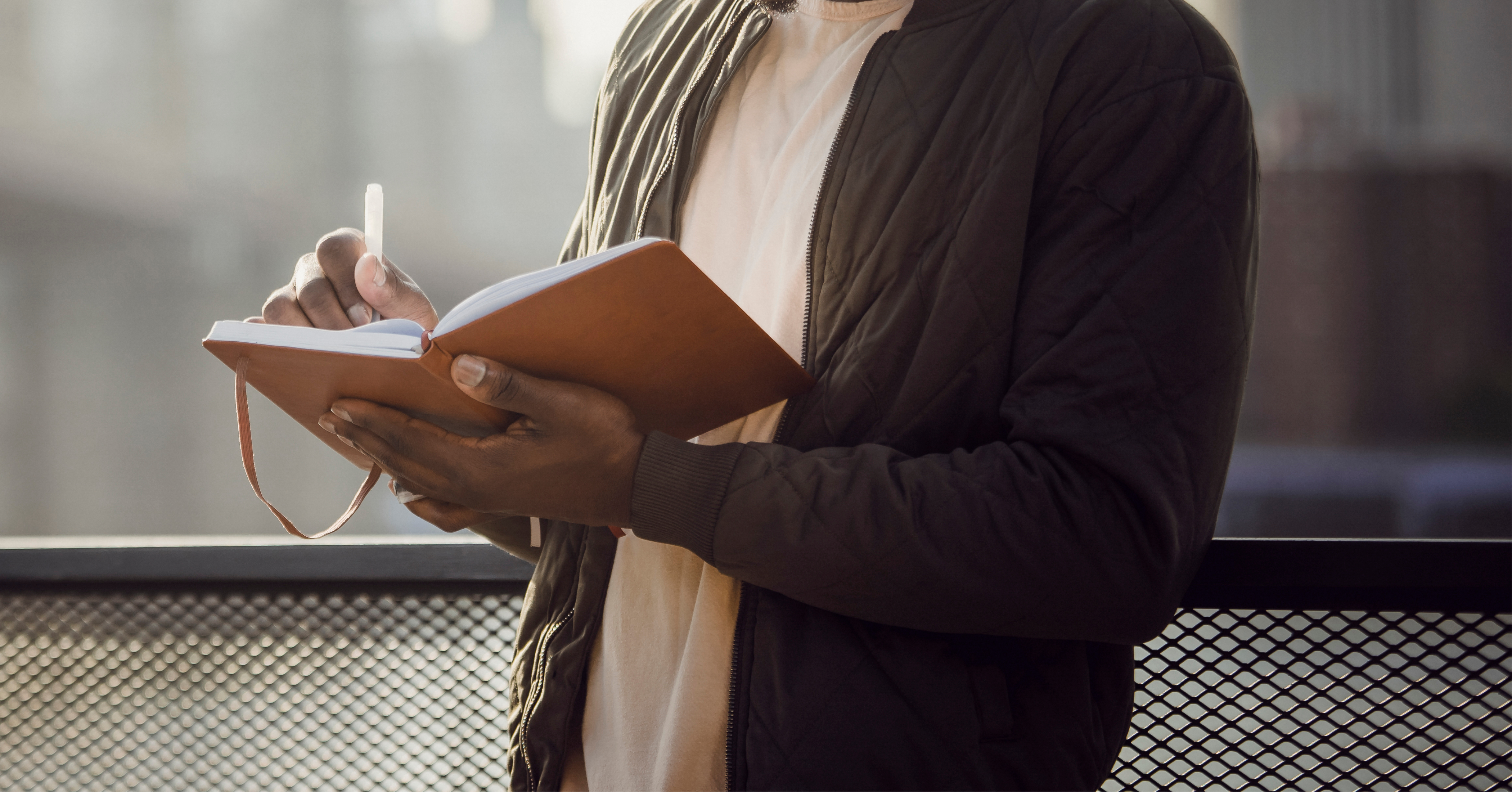 man standing on a bridge writing in a notebook