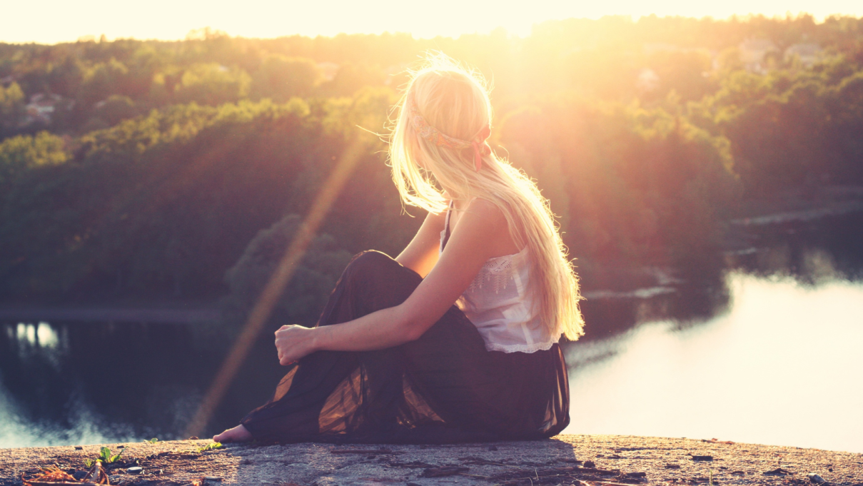 woman sitting on a cliff looking over the water