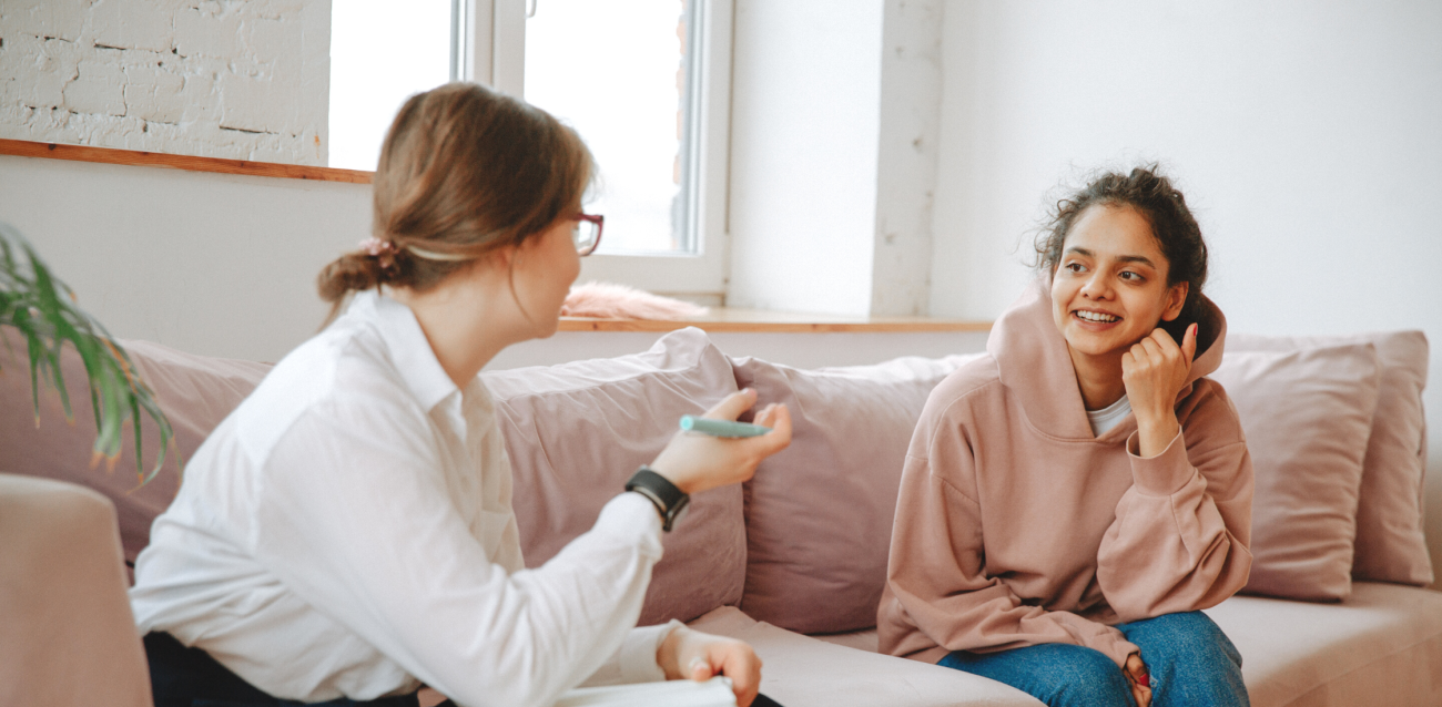 A therapist and a teenage girl sitting on a couch having a conversation