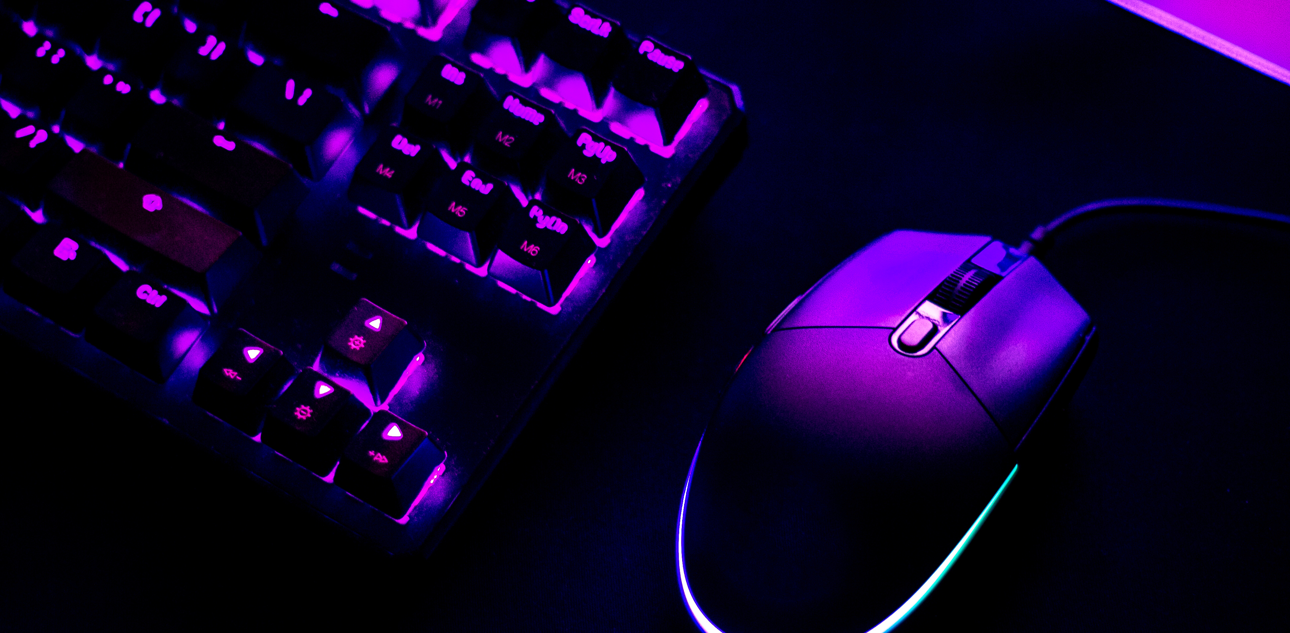 A keyboard and mouse in a dark room lit up with purple backlights